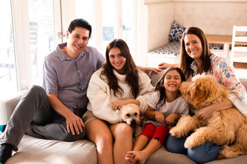 Family of four smiling at the camera sitting on the couch with their pet dogs at home