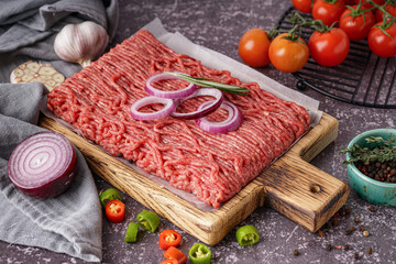 Wooden board of fresh minced meat with spices on grey background