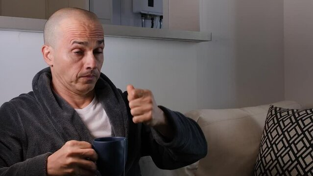 48 year old Brazilian man with his hand over his eyes, frustrated and drinking a cup of tea.