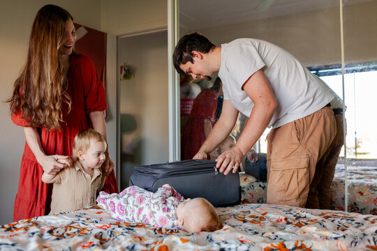 Family together in bedroom packing bag for holidays zipping up suitcase