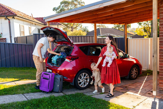 Dad in his twenties packing bags and suitcases into car boot for weekend away with kids