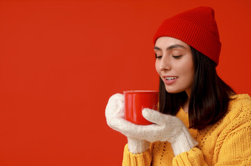 Beautiful young woman with cup of hot mulled wine on red background