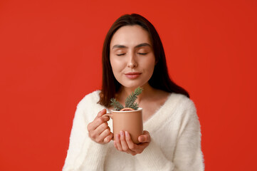 Beautiful young woman with cup of hot mulled wine on red background
