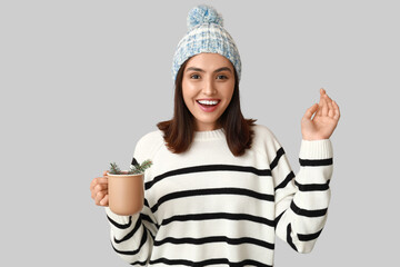 Happy young woman with cup of hot mulled wine on grey background