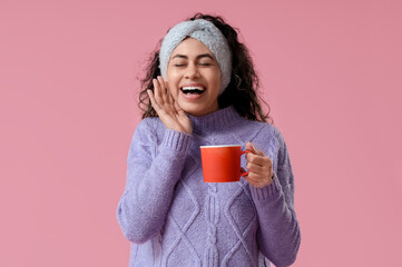 Happy young African-American woman with cup of hot mulled wine on pink background