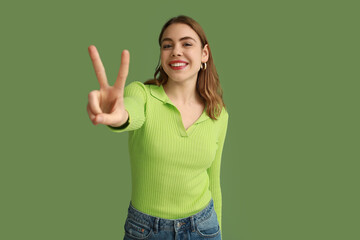 Pretty young woman showing peace gesture on green background