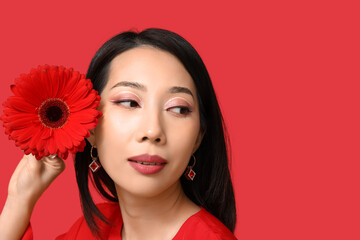 Pretty young Asian woman with beautiful gerbera flower on red background