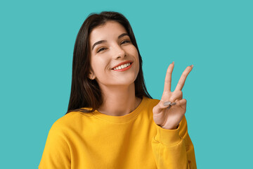 Young woman showing peace sign on blue background, closeup