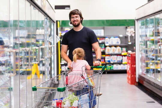 Dad with toddler in shopping trolley buying groceries at shops in cold food aisle