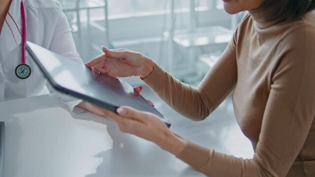 Doctor presenting information tablet to woman at medical consultation closeup.