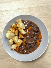 A bowl of beef stew with roast potato.