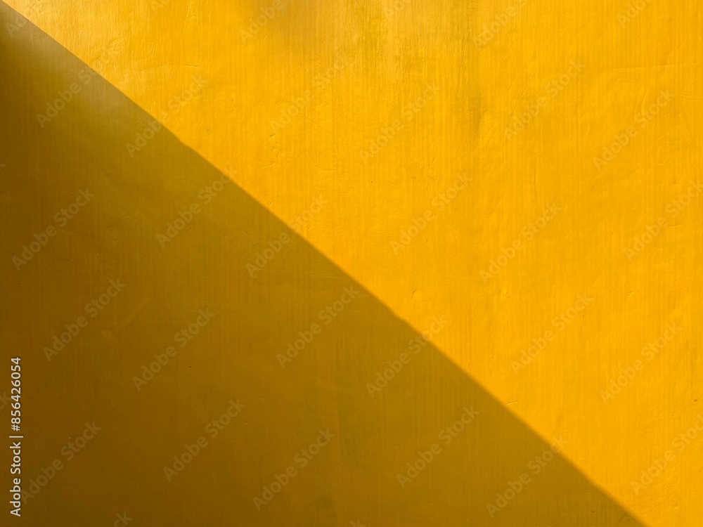 Poster a yellow wall with a shadow. the wall is made of concrete and has a rough texture. the shadow is cas