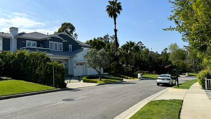 generic American residential neighborhood - broad road with sidewalk, single-family home, car, trees and grassy lawns - Encino, Los Angeles, California