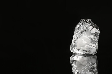 Piece of clear ice on black mirror surface, space for text
