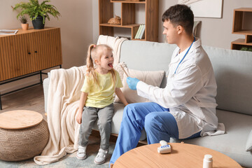 Obraz premium Male pediatrician examining little girl with tongue depressor at home