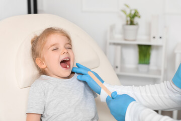 Pediatrician examining little girl with tongue depressor in clinic
