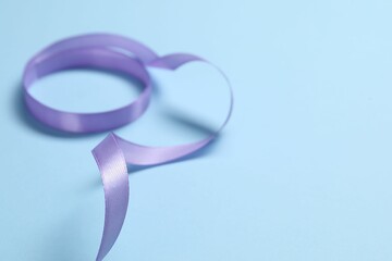 Beautiful violet ribbon on light blue background, closeup. Space for text