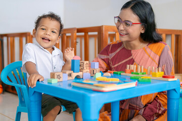 Young Latin mom tickles her little son at home, while they play and learn with colorful educational games for childhood learning