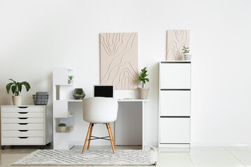 Interior of light office with modern workplace, laptop and pictures