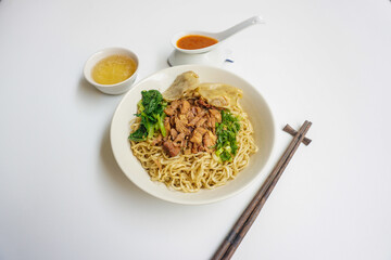Mie Ayam Pangsit (Noodles with Chicken, Dumplings and vegetables ) is Indonesian popular food. Served in bowl on white table. Selective focus.
