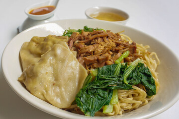 Mie Ayam Pangsit (Noodles with Chicken, Dumplings and vegetables ) is Indonesian popular food. Served in bowl on white table. Selective focus.