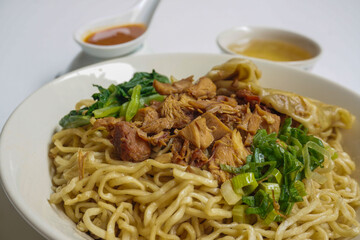 Mie Ayam Pangsit (Noodles with Chicken, Dumplings and vegetables ) is Indonesian popular food. Served in bowl on white table. Selective focus.