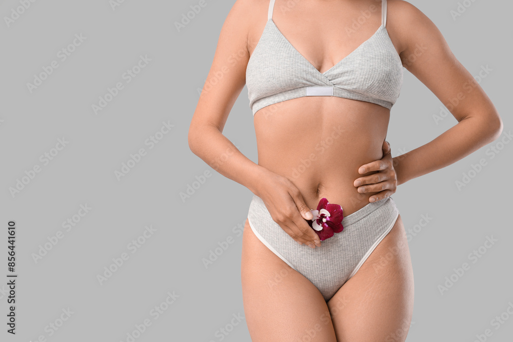 Wall mural young woman in underwear with beautiful orchid flower on grey background