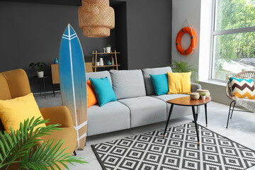Comfortable sofa, armchair and surfboard in interior of living room