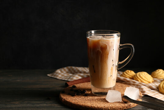 Glass cup of iced latte with coffee beans and sweet cookies on wooden table