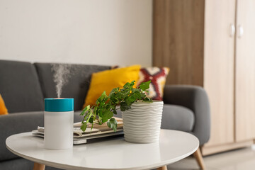 Air humidifier with plant and magazines on table in living room, closeup