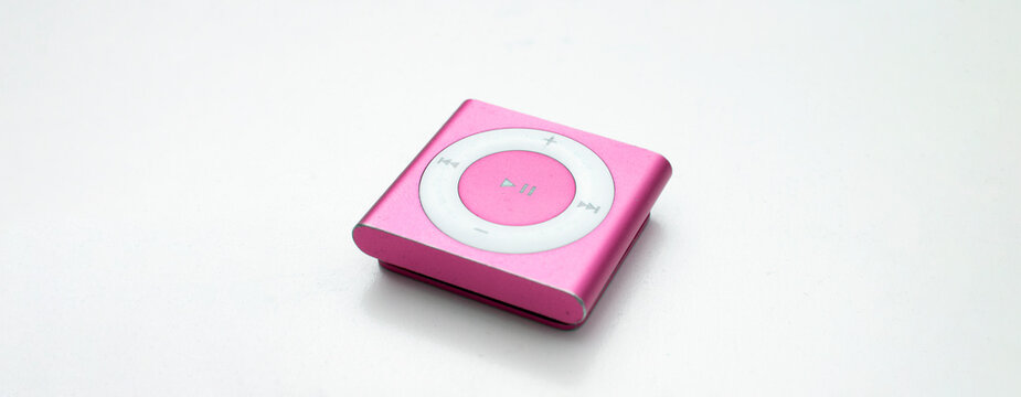 Saint-Petersburg, Russia - May 9, 2022: Pink small metal square old music player iPod Shuffle with big round button on white background close up. Vintage, technique, technology, song, sing. Copy space