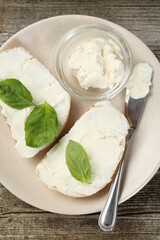 Delicious sandwiches with cream cheese and basil leaves on wooden table, top view