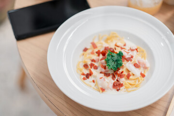 Close-up of a creamy pasta dish topped with crispy bacon bits and fresh parsley, served on a white...
