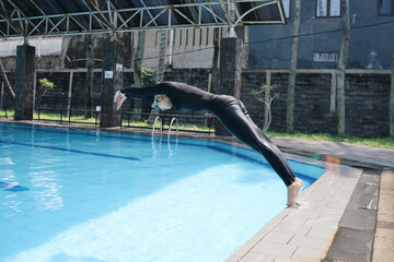Full Length Of Young Asian Sportswoman In Swimwear Showing Jumping Technique To The Pool