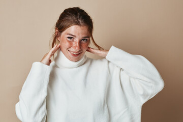 Smiling young woman in white turtleneck sweater portrait on beige background for fashion beauty concept