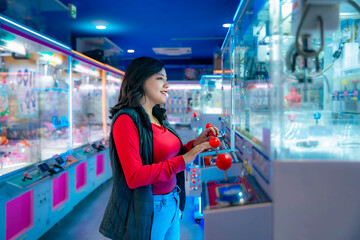 Young Latina woman smiling and playing arcade games in Akihabara, Tokyo, Japan, surrounded by...