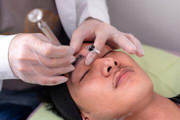 An esthetician using a microblade tool to make small cuts into the eyebrow of a customer. A Microblading technique to implant pigment. Male brow enhancement.