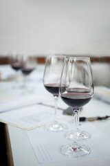 Red wine glasses are on a table with blurred tasting notes in a degustation room