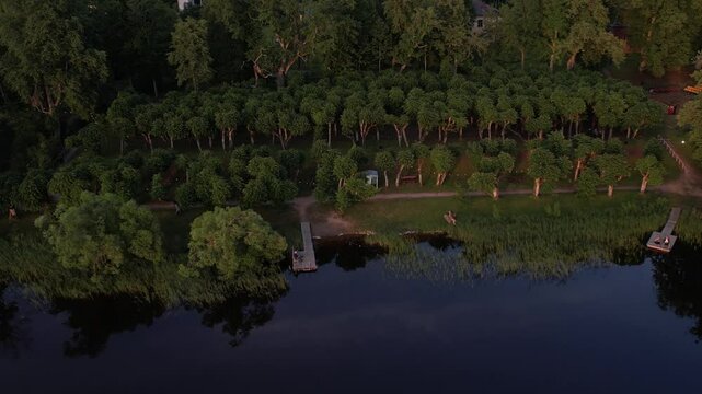 A stunning drone view of Katvari village at sunset, highlighting the Katvari linden tree by the lake. The golden sunlight casts a warm glow over the tranquil water.