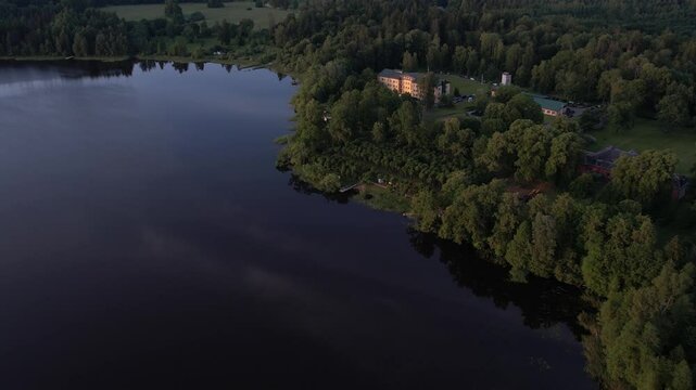 A stunning drone view of Katvari village at sunset, highlighting the Katvari linden tree by the lake. The golden sunlight casts a warm glow over the tranquil water.