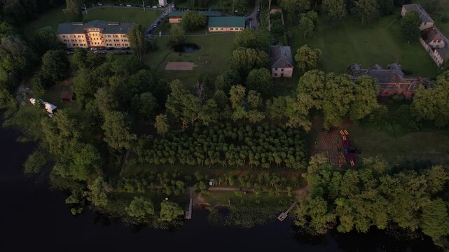 A stunning drone view of Katvari village at sunset, highlighting the Katvari linden tree by the lake. The golden sunlight casts a warm glow over the tranquil water.