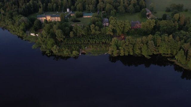 A stunning drone view of Katvari village at sunset, highlighting the Katvari linden tree by the lake. The golden sunlight casts a warm glow over the tranquil water.