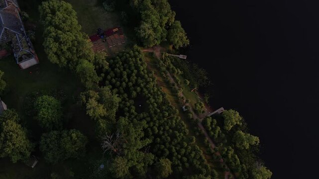 A stunning drone view of Katvari village at sunset, highlighting the Katvari linden tree by the lake. The golden sunlight casts a warm glow over the tranquil water.