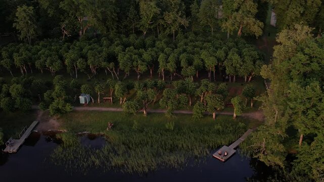 A stunning drone view of Katvari village at sunset, highlighting the Katvari linden tree by the lake. The golden sunlight casts a warm glow over the tranquil water.