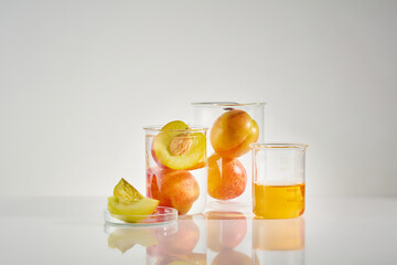 Different size glass beakers containing ripe peach and essence of peach, displayed on white laboratory countertop, against white background. Front view photo, space for designing