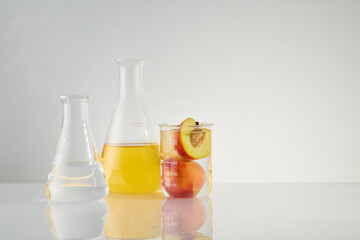 Advertising photo for cosmetic or beauty care products, which natural composition like peach. Two beakers filled by yellow and transparent liquid placed by side, next to a beaker of soaked peach