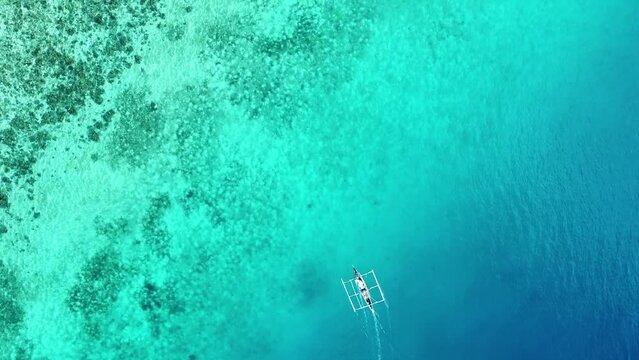 traditional philippine wooden fishing boat sailing over a coral reef in the crystal clear water of the ocean aerial view