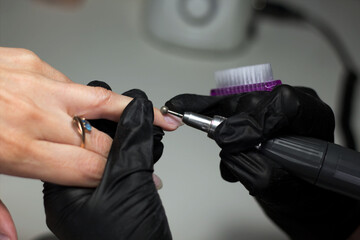 A nail technician, wearing black gloves, uses an electric nail drill for precision work on a client’s nail. 