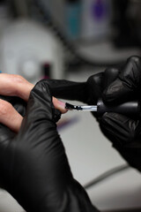 Black-gloved nail technician meticulously applying clear nail polish on client’s nails. The image captures the precision and care typical of professional nail salon services.