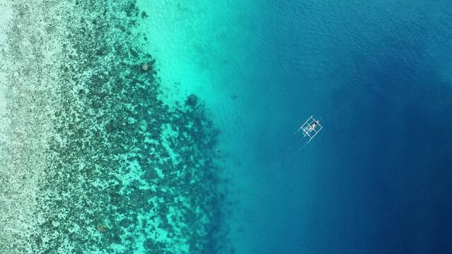 traditional philippine wooden fishing boat sailing over a coral reef in the crystal clear water of the ocean aerial view